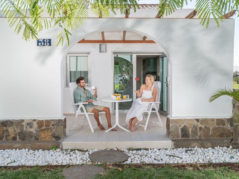 Coppia rilassata su sedie davanti a una casa vacanze bianca con base in pietra e prato verde.