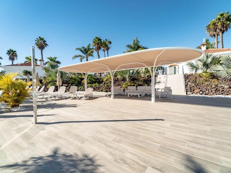 Ombreggiatura moderna su una terrazza con palme in un giardino di un hotel soleggiato.