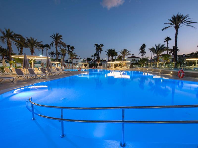 Piscina illuminata con lettini e palme in un resort hotel al crepuscolo.