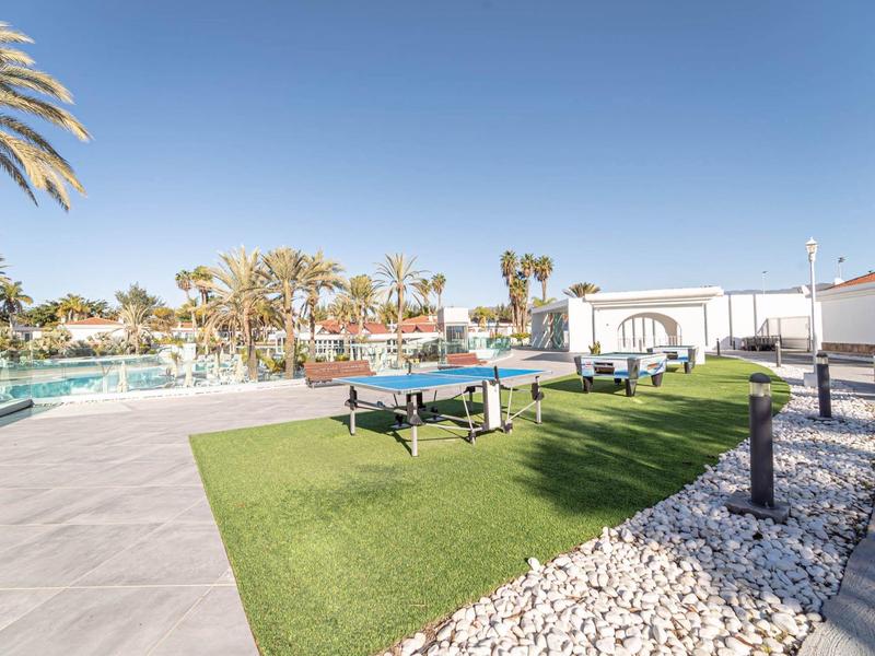 Area esterna con tavoli da ping pong, piscina e lettini sotto un cielo limpido.