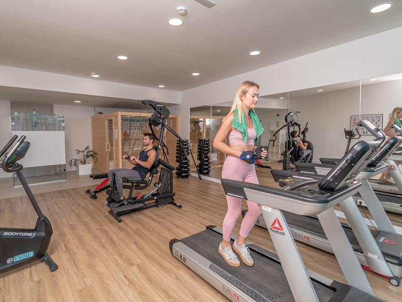 Due persone si allenano in una palestra luminosa con pavimento in legno e vari attrezzi da palestra.