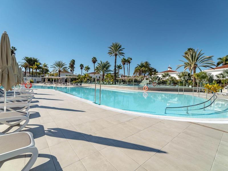 Ampia area piscina invitante con lettini e palme sotto un cielo azzurro limpido.