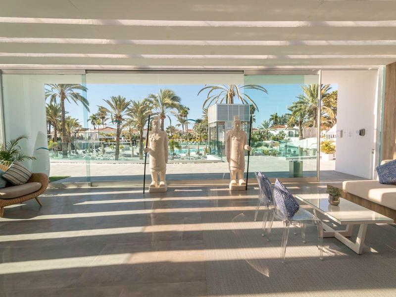 Grande stanza con vista sulla piscina e palme attraverso una facciata di vetro in un hotel.