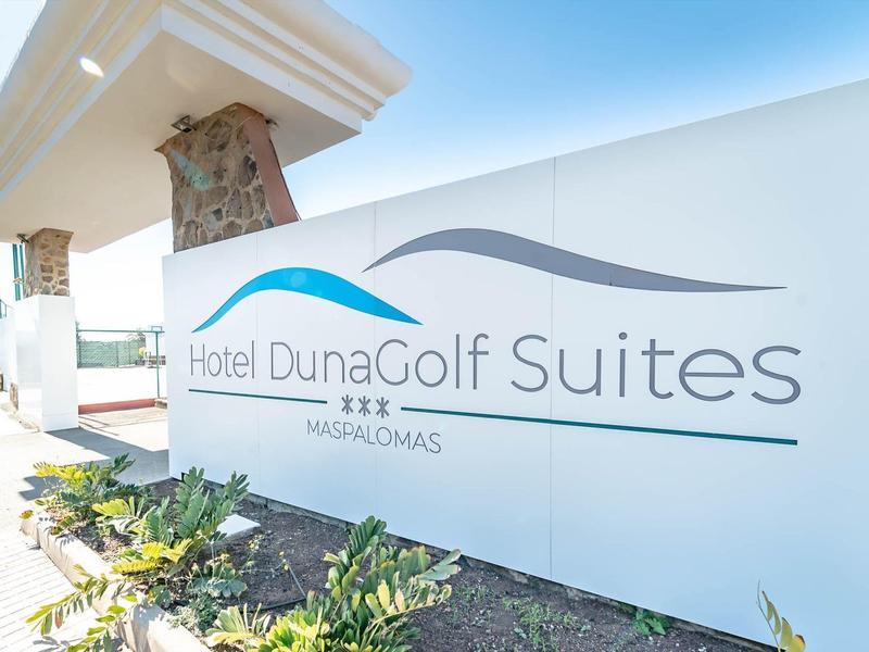 Insegna d'ingresso dell'hotel DunaGolf Suites con muri bianchi e piante in primo piano