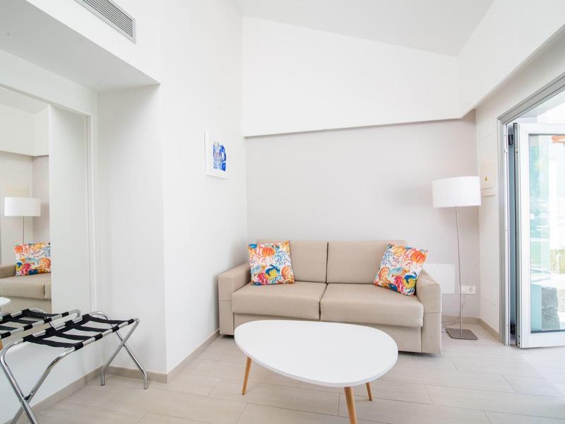 Soggiorno luminoso con divano grigio, tavolo bianco rotondo e accesso al balcone.