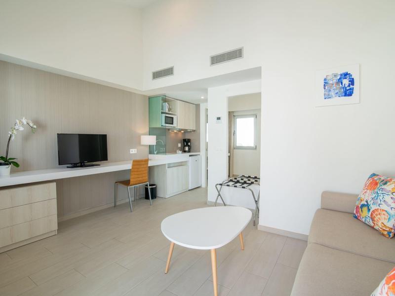 Soggiorno luminoso con divano, tavolino, scrivania e cucina aperta in un appartamento per vacanze.