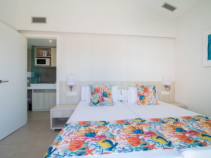 Camera luminosa con letto grande, copriletto colorato e bagno aperto.