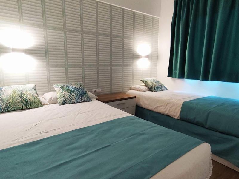 Pokój hotelowy z dwoma łóżkami, nowocześnie urządzony z białymi ścianami i niebieskimi zasłonami.