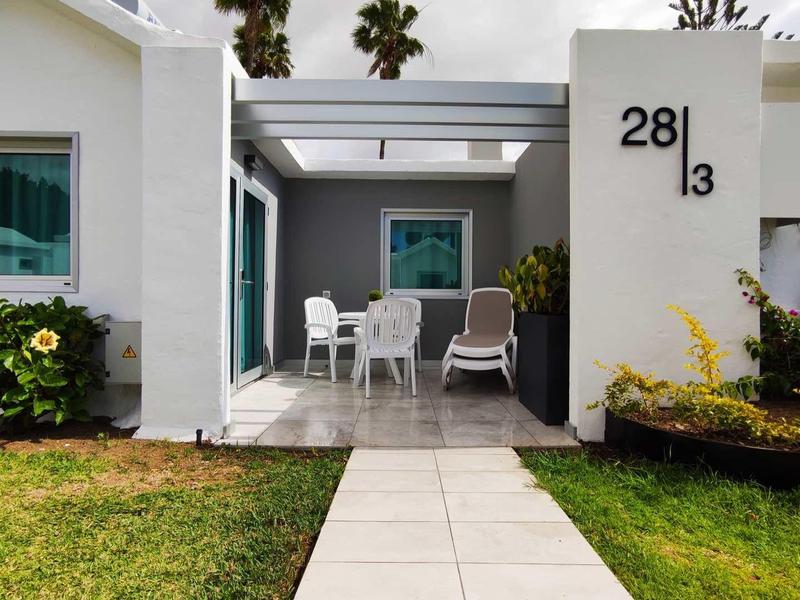 Nowoczesny biały bungalow z werandą, ogrodem i leżakiem w świetle dziennym.