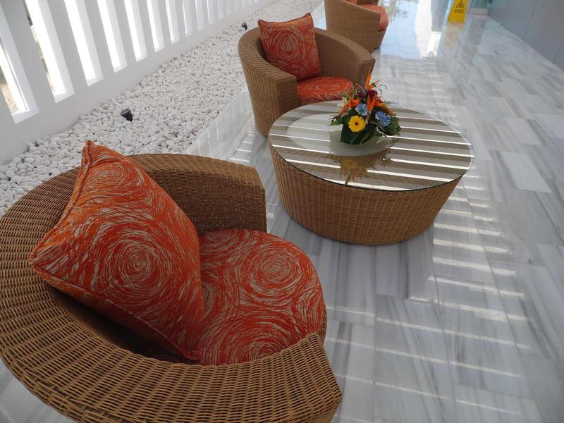Dwa okrągłe wiklinowe fotele z pomarańczowymi poduszkami i okrągły stolik z kwiatami na marmurowym tarasie.