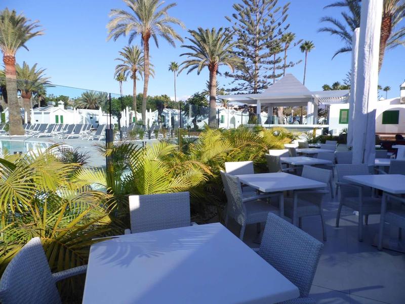 Restauracja na świeżym powietrzu z białymi stołami i krzesłami obok basenu i palm.