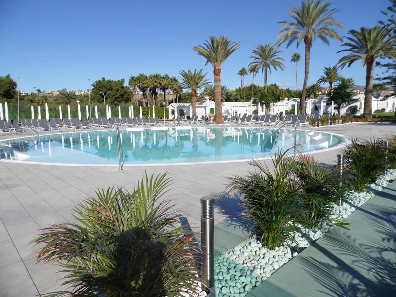 Okrągły basen hotelowy otoczony palmami i białymi leżakami pod czystym niebem.