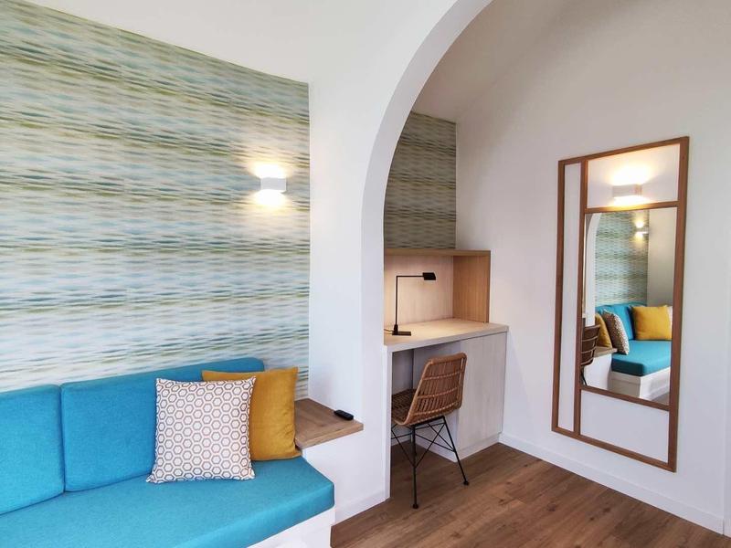 Nowoczesny pokój hotelowy z niebieską sofą, kolorowymi poduszkami i miejscem do pracy pod łukiem.