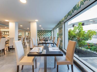 Helles, modernes Restaurant mit großen Fenstern und Blick auf grünen Innenhof, gedeckte Tische.