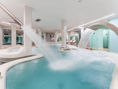 Moderner Innenpool mit Wasserfontänen, runden Becken und hellem, minimalistischem Design.