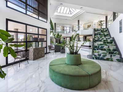 Heller Empfangsbereich mit weißem Marmorboden, grüner Sitzinsel und vielen Pflanzen.