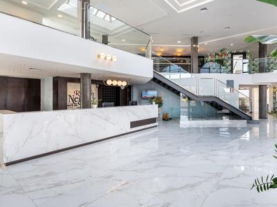 Helle Empfangshalle mit weißem Marmorboden, Rezeptionstresen und moderner Glas-Treppenanlage.