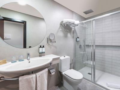 Moderner Badezimmer mit ovalem Spiegel, weißem Waschbecken, Toilette und Glaskabine für Dusche.