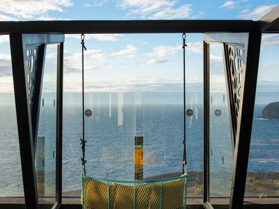 Moderní houpačka s výhledem na moře pod modrou oblohou s mraky.