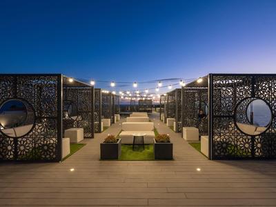 Moderner, beleuchteter Außenbereich mit Sitzbänken, dekorativen Metallwänden und blauem Abendhimmel.