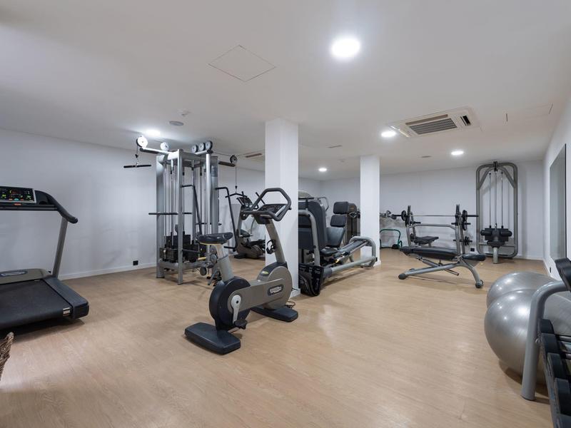 Moderner Fitnessraum mit verschiedenen Trainingsgeräten und hellen Wänden, Holzboden und Deckenlichtern.