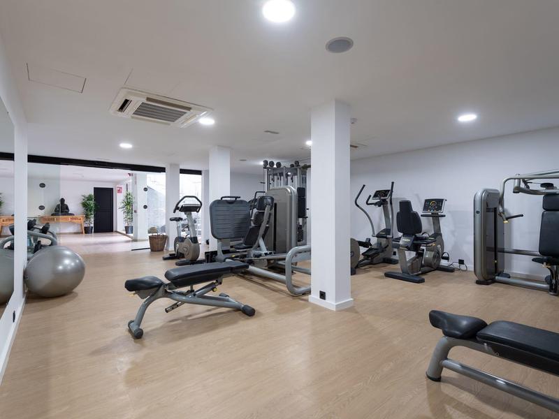 Heller Fitnessraum mit vielen Trainingsgeräten, Spiegelwand und Holzboden.