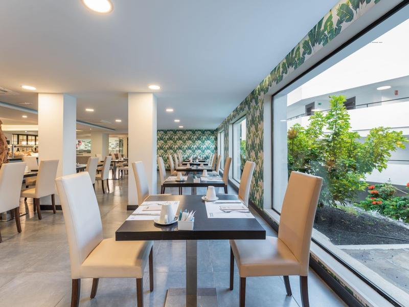 Helles, modernes Restaurant mit großen Fenstern und Blick auf grünen Innenhof, gedeckte Tische.