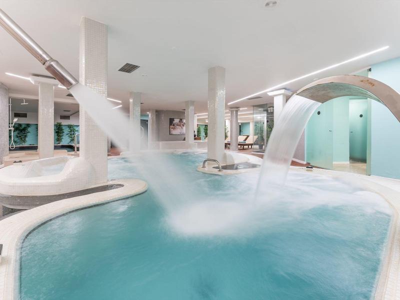 Moderner Innenpool mit Wasserfontänen, runden Becken und hellem, minimalistischem Design.