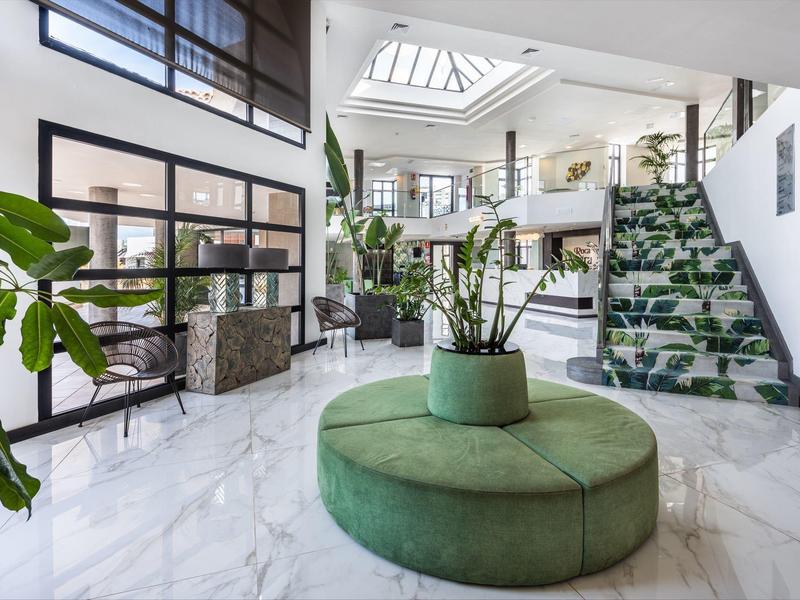 Heller Empfangsbereich mit weißem Marmorboden, grüner Sitzinsel und vielen Pflanzen.