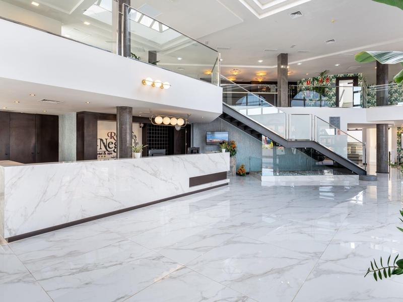 Helle Empfangshalle mit weißem Marmorboden, Rezeptionstresen und moderner Glas-Treppenanlage.