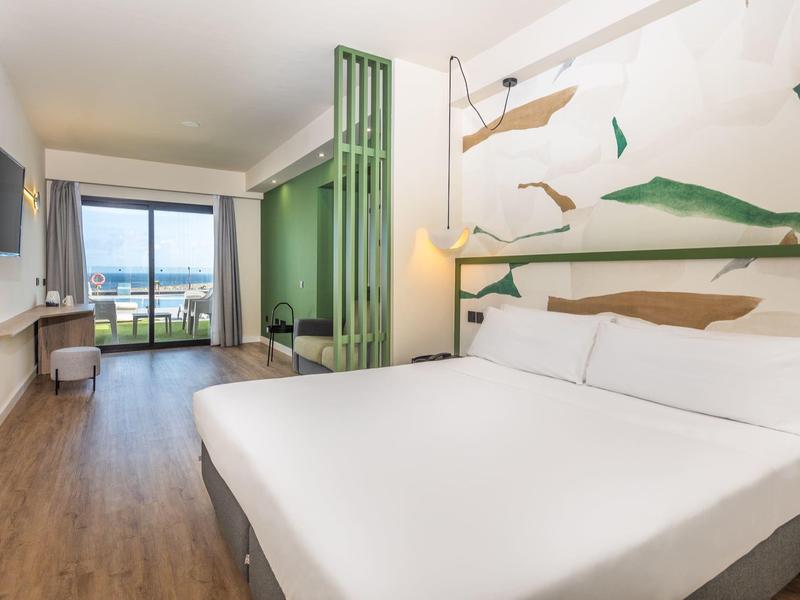 Helles, modernes Schlafzimmer mit großem Bett, Holzfußboden, Wandkunst und Meerblick vom Fenster.