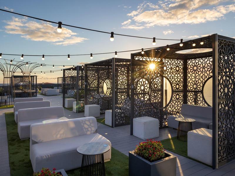 Dachterrasse mit Sitzmöbeln aus Rattan, hängenden Lichtern und dekorativen Trennwänden bei Sonnenuntergang.