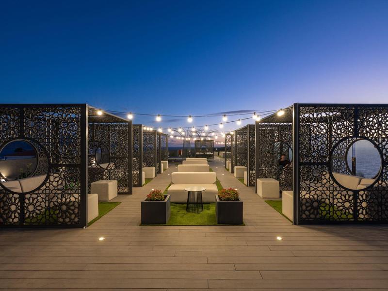 Moderner, beleuchteter Außenbereich mit Sitzbänken, dekorativen Metallwänden und blauem Abendhimmel.