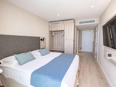 Camera d'hotel moderna con letto matrimoniale, testiera grigia e armadio aperto.