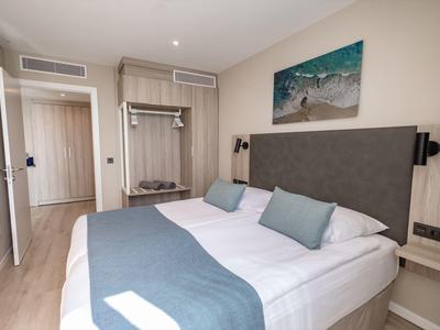 Camera d'albergo moderna con letto grande, testiera grigia e biancheria da letto blu-grigia.