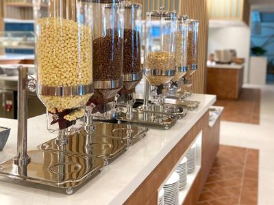 Quattro distributori con diversi cereali per la colazione su un bancone buffet in hotel.