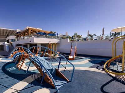 Un'area giochi moderna e colorata con strutture per arrampicarsi e altalene sotto un cielo sereno.