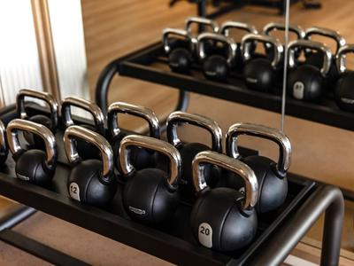 Kettlebelle o różnych wagach ułożone na stojaku z lustrem w tle.