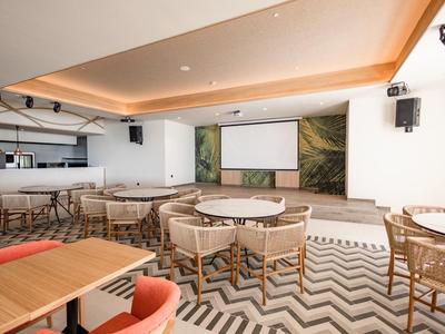 Sala eventi moderna con area salotto, bar e grande schermo di proiezione.