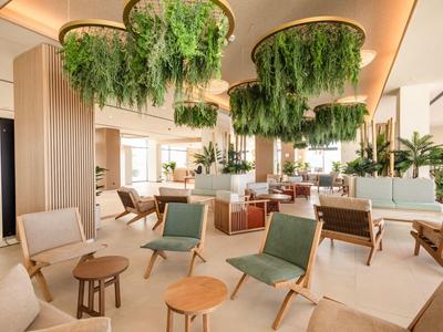 Lounge di hotel moderna e luminosa con piante verdi, poltrone comode e vegetazione sospesa al soffitto.