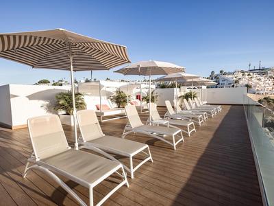 Taras na dachu z leżakami, parasolami i szklaną balustradą pod czystym niebem