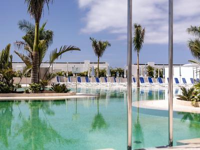 Piscina esterna invitante con palme e lettini sotto un cielo azzurro.