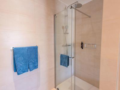 Area doccia moderna con porta in vetro, doccia a pioggia e asciugamano blu in bagno.