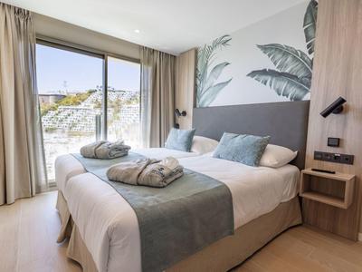 Camera d'hotel moderna con letto matrimoniale, grandi finestre e decorazioni a tema natura.