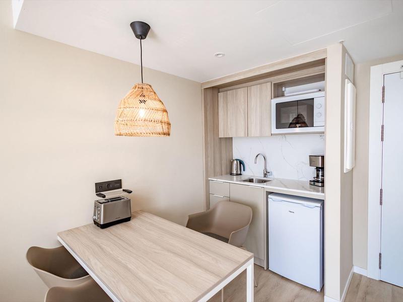 Piccola angolo cottura con tavolo, due sedie e lampada in legno in una camera d'hotel.