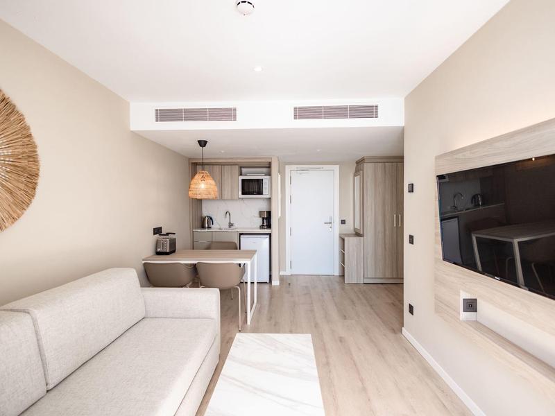 Camera d'hotel moderna e luminosa con divano, TV e angolo cottura piccolo.