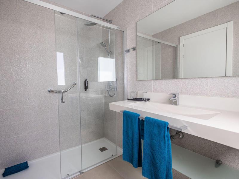 Area bagno moderna con doccia in vetro, grande specchio e due asciugamani blu.