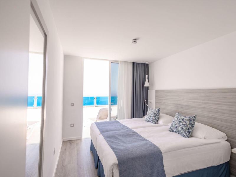 Camera d'hotel luminosa con due letti, accenti blu e vista mare.