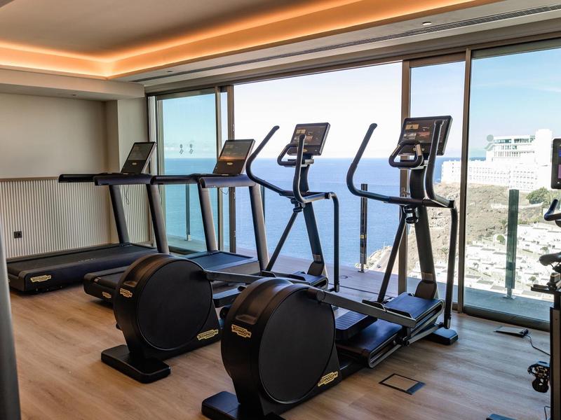 Palestra moderna con tapis roulant e macchine ellittiche davanti a grandi finestre con vista.