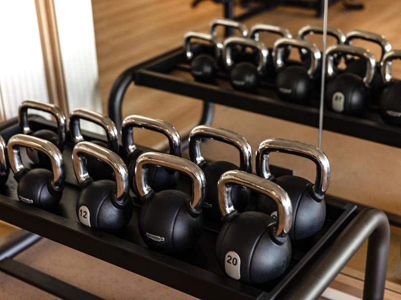 Fila di kettlebell nere con maniglie argento su uno scaffale davanti a uno specchio.